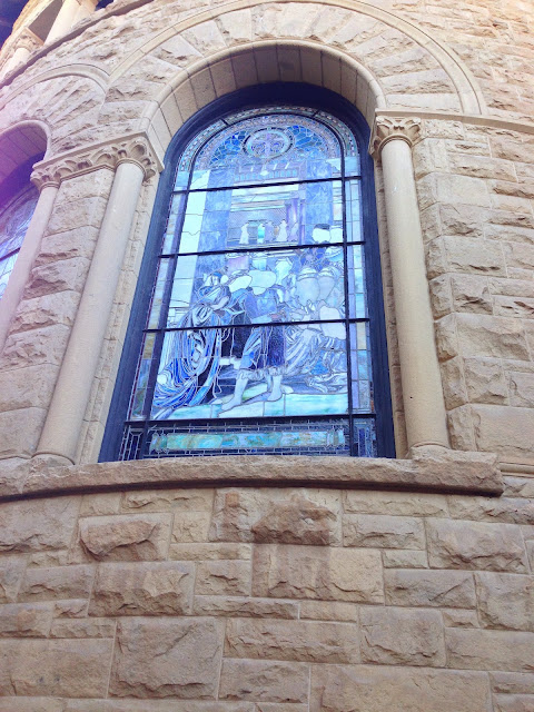 A bold charcoal drawing of an arched stained-glass window above stone columns, deep purple and midnight tones with warm gold highlights, evoking a stadium atmosphere.